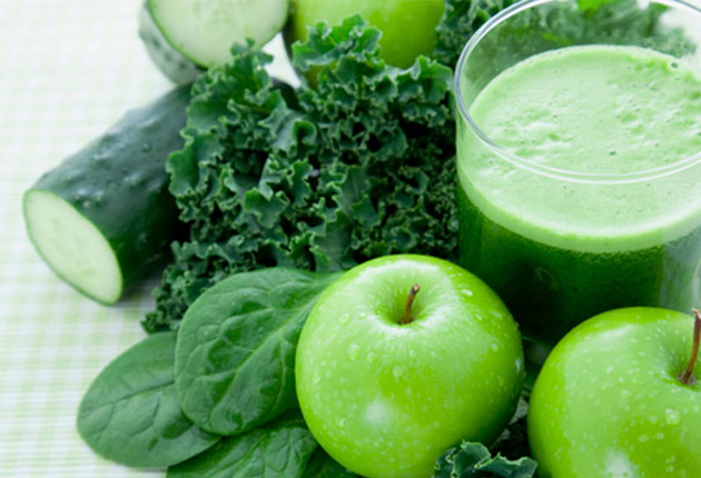 Licuado verde y junto a frutas y verduras. 